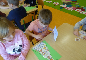 Dwoje dzieci wspólnie układają piramidę zdrowia z wykorzystaniem obrazków z produktami spożywczymi.